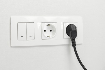 Electrical sockets on the wall with black connection plug and white switch.