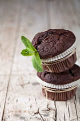 Chocolate dark muffins with mint leaves on rustic wooden table.