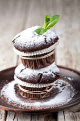 Wall Mural - Fresh chocolate dark muffins with sugar powder and mint leaf on brown plate.