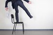 Businessman balancing while standing on an office chair against the wall with space for text.