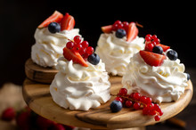 Four Homemade White Mini Desserts Pavlova On Wooden Board With Whipped Cream, Cut Strawberries, Blueberries, Red Currants 