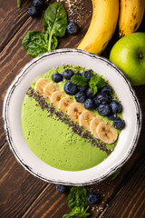 Breakfast detox green smoothie bowl from banana and spinach on wooden background. Healthy food concept, top view