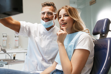 Photo of joyful woman sitting in medical chair at dental clinic while doctor fixing her teeth