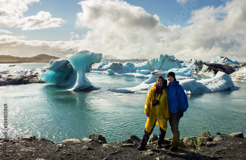 Cuadros en Lienzo Young beautiful happy couple of girl and guy staying on the coast with blue ices in the background in Iceland near the lake with ice floes, in Jokursarlon, on a diamond beach