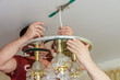 Men repair, install and remove the chandelier with a screwdriver in the house. Service for repair, installation and removal of chandeliers. Disassembled suspended chandelier with bare wires