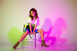 © LIGHTFIELD STUDIOS - attractive young woman sitting on chair and holding sunglasses on purple with gradient