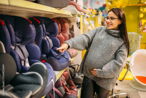 Fotografía Pregnant woman choosing child car seat in store