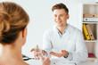 © LIGHTFIELD STUDIOS - selective focus of cheerful doctor gesturing while holding box with pills near patient