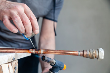 Wall Mural - Closeup professional master plumber holding flux paste for soldering and brazing seams of copper pipe gas burner. Concept installation and repair of an apartment building pipeline, leakage