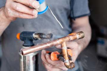 Wall Mural - Closeup professional master plumber holding flux paste for soldering and brazing seams of copper pipe gas burner. Concept installation and repair of an apartment building pipeline, leakage