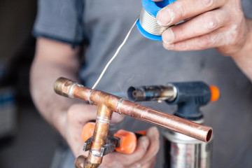 Wall Mural - Closeup professional master plumber holding flux paste for soldering and brazing seams of copper pipe gas burner. Concept installation and repair of an apartment building pipeline, leakage