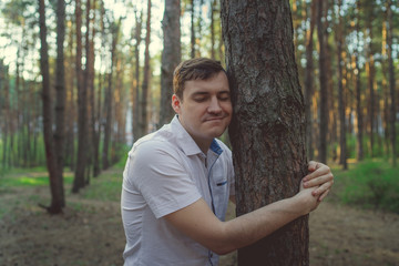 Man hugging tree in the forest. Smiling young male nature lover relax on summer day hug a tree enjoy in beautiful day	