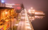 Fototapeta Miasto - Very foggy night, view from the bridge to the embankment of Umea river, the old side of central Umea city, Vasterbotten municipality, Sweden