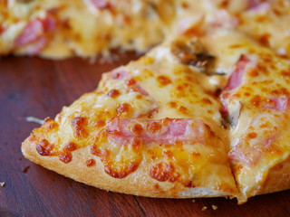 Close up and selective focus of well-done fresh appetizing mushroom, ham, cheese pizza being served on a wooden tray, ready to eat