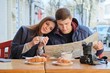 © Valerii Honcharuk - Young beautiful couple of tourists resting in outdoor cafe, reading city map, drinking coffee with croissants.