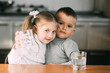 © komokvm - Children boy and girl in the kitchen drinking water from glasses, hugging and smiling
