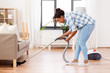 household and housework concept - happy african american woman or housewife with vacuum cleaner cleaning floor under sofa at home