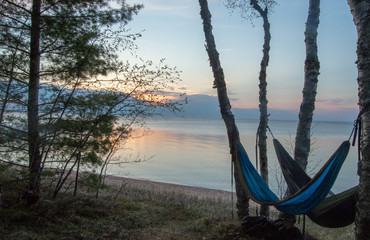 two hammocks set up between trees overlooking a sunset on lake superior in northern michigan.