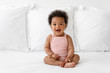 © Lisa Tichané - Smiling baby with afro hair sitting on bed