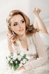 Wall Mural - Beautiful girl with blond hair in a bright room is lying on the floor. Bride lying holding a bouquet