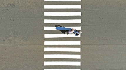 Two pedestrians: man and woman crossing zebra crosswalk, aerial, top view