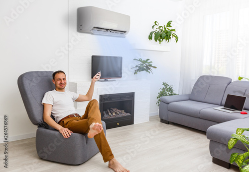 man turning on air conditioner with remote control while using laptop on sofa