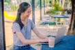 © TeTe Song - Young smiling hipster girl using laptop for work while sitting on a table in the park , Female student studying at park and using modern laptop at sunny day