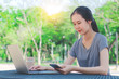 © TeTe Song - Young girl is a university student with cup of coffee and a phone in her hands working on a laptop at the table in the park. The concept of shopping online in the Internet