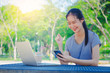 © TeTe Song - Successful young girl is a university student with cup of coffee and a phone in her hands working on a laptop at the table in the park. The concept of shopping online in the Internet