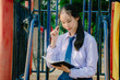 © TeTe Song - Lovely teenage girl wearing school uniform writing book while thinking with sitting on a swing at the park,Nature, education, outdoor and study concept..