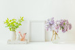 Home interior with decor elements. White frame, branches of lilac in a vase, cosmetic set