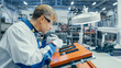 © Gorodenkoff - Man in Blue Work Coats is Using Tweezers to Assemble Printed Circuit Boards for Smartphones. Electronics Factory Workers in a High Tech Factory Facility.