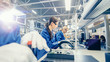 Female Electronics Factory Worker in Blue Work Coat and Protective Glasses is Assembling Laptop's Motherboard with a Screwdriver. High Tech Factory Facility with Multiple Employees. 