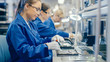 © Gorodenkoff - Female Electronics Factory Worker in Blue Work Coat and Protective Glasses is Assembling Laptop's Motherboard with a Screwdriver. High Tech Factory Facility with Multiple Employees.