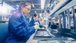 © Gorodenkoff - Woman Electronics Factory Worker in Blue Work Coat and Protective Glasses is Assembling Laptop's Motherboard with a Screwdriver. High Tech Factory Facility with Multiple Employees.