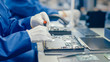 © Gorodenkoff - Close-Up of a Female Electronics Factory Worker in Blue Work Coat Assembling Laptop's Motherboard with a Screwdriver. High Tech Factory Facility with Multiple Employees.