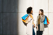 © Westend61 - Two happy women with shopping bags standing at a wall talking