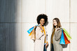 © Westend61 - Portrait of two happy women with shopping bags standing at a wall