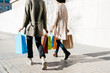 © Westend61 - Portrait of two happy women with shopping bags walking along a wall in the city