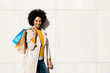 © Westend61 - Portrait of smiling woman with shopping bags standing at a wall