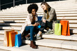 © Westend61 - Two happy women with shopping bags sitting on stairs using cell phone