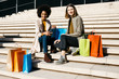 © Westend61 - Portrait of two happy women with shopping bags sitting on stairs