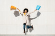 © Westend61 - Cheerful woman with shopping bags jumping at a wall
