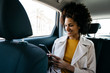 © Westend61 - Smiling woman sitting in back seat of a car using cell phone