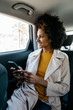 © Westend61 - Smiling woman sitting in back seat of a car holding cell phone