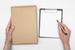 © Dmitriy - A parcel cardboard box in a delivery boy hands and a blank invoice document mock up on a white wooden table background. Delivery service concept.