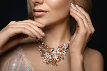 Beautiful young woman with elegant jewelry on dark background, closeup