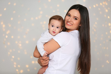 Wall Mural - Portrait of young mother and her adorable baby against defocused lights