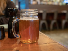 Mason Jar Mug With Handle Filled With Beer Next To Sake Bottle At Restaurant