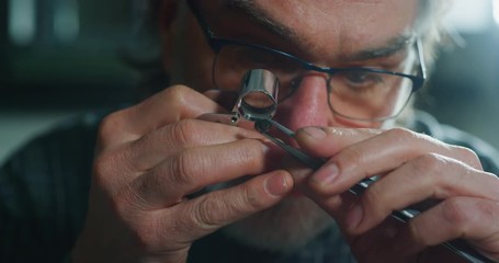 Wall Mural - Slow motion macro close up of experienced goldsmith controlling a quality of precious gem, selected for making jewels in workshop. Shot in 8K. Concept of jewelry,luxury,goldsmith, diamonds, brilliance